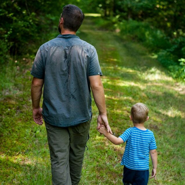 Man holding child's hand, walking down a forest path