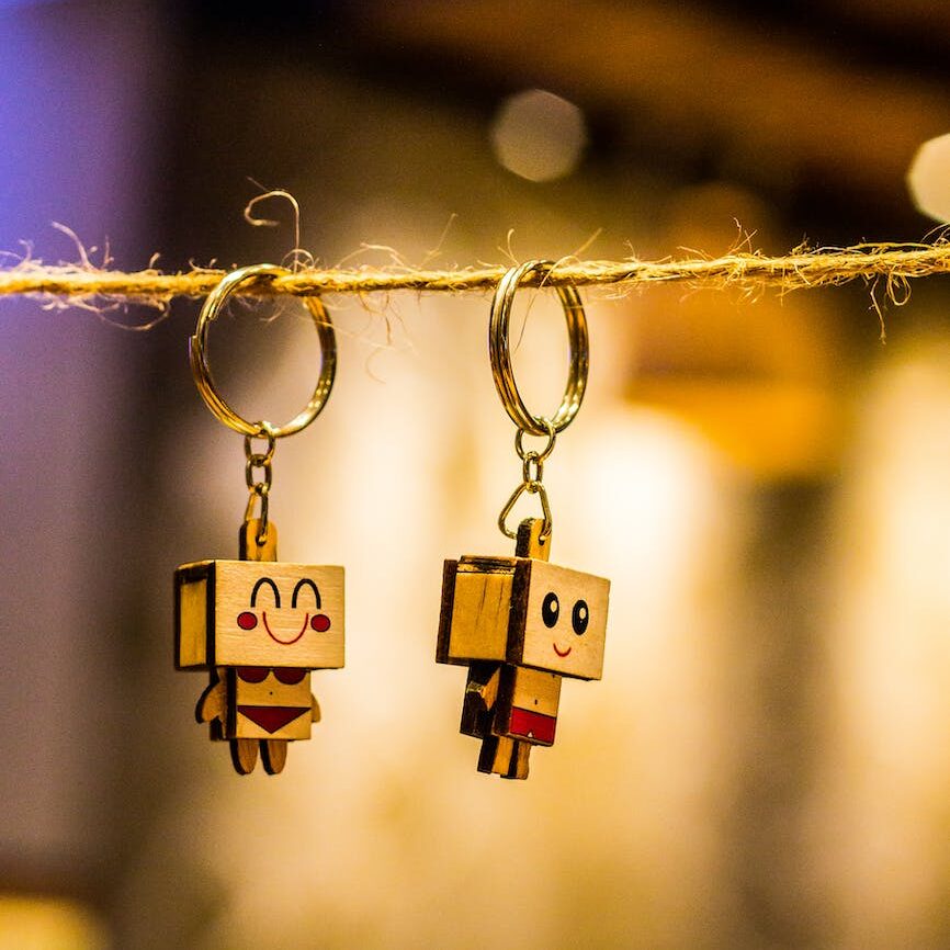 bokeh photography of two wood block man and woman figure key chains hanging on brown thread